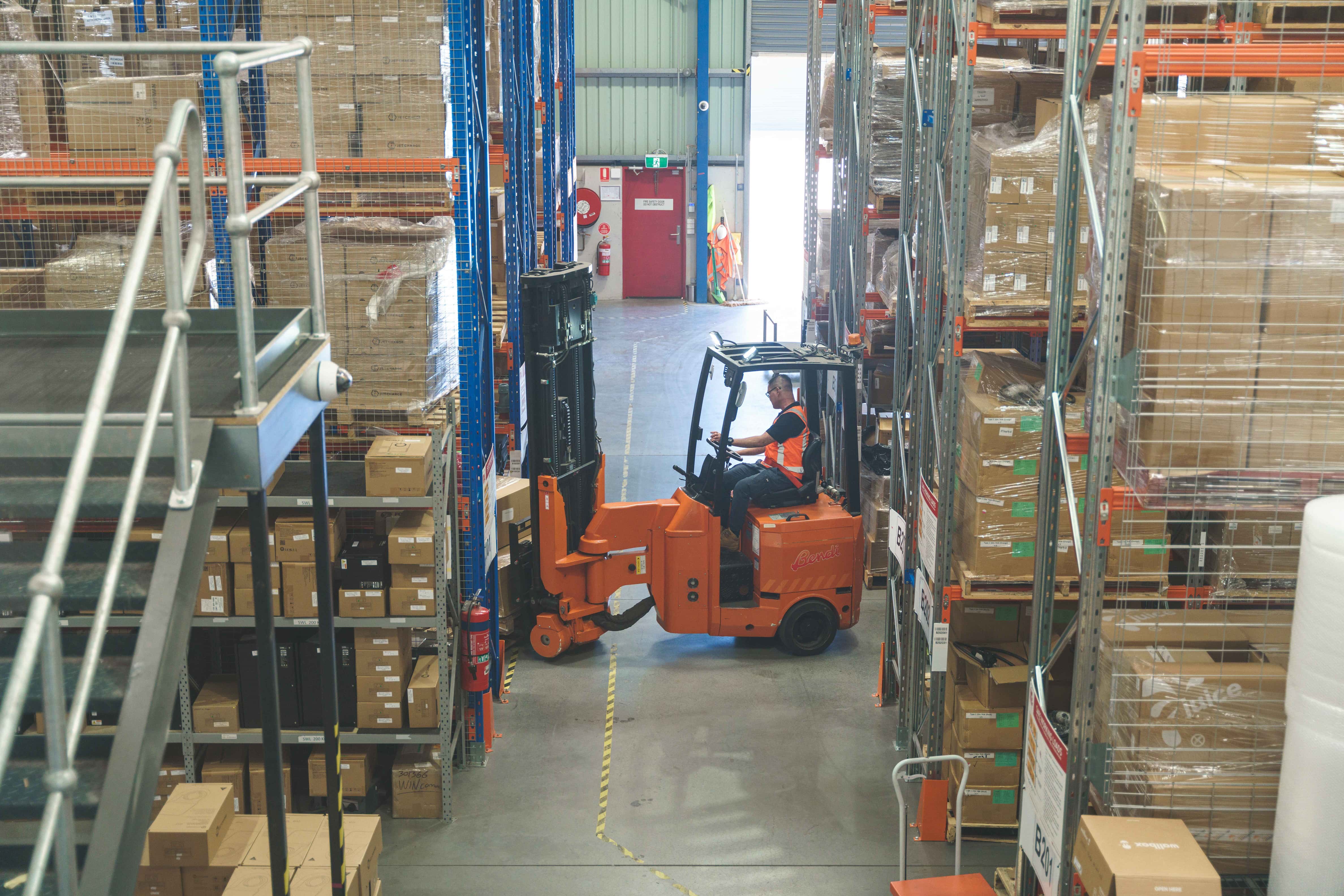 A forklift manoeuvring through a warehouse, with EV charging infrastructure visible in the background.