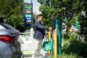 A man wearing a blazer unplugs a JET Charge plus EV charger from its charging station to charge his car while he shops for groceries.