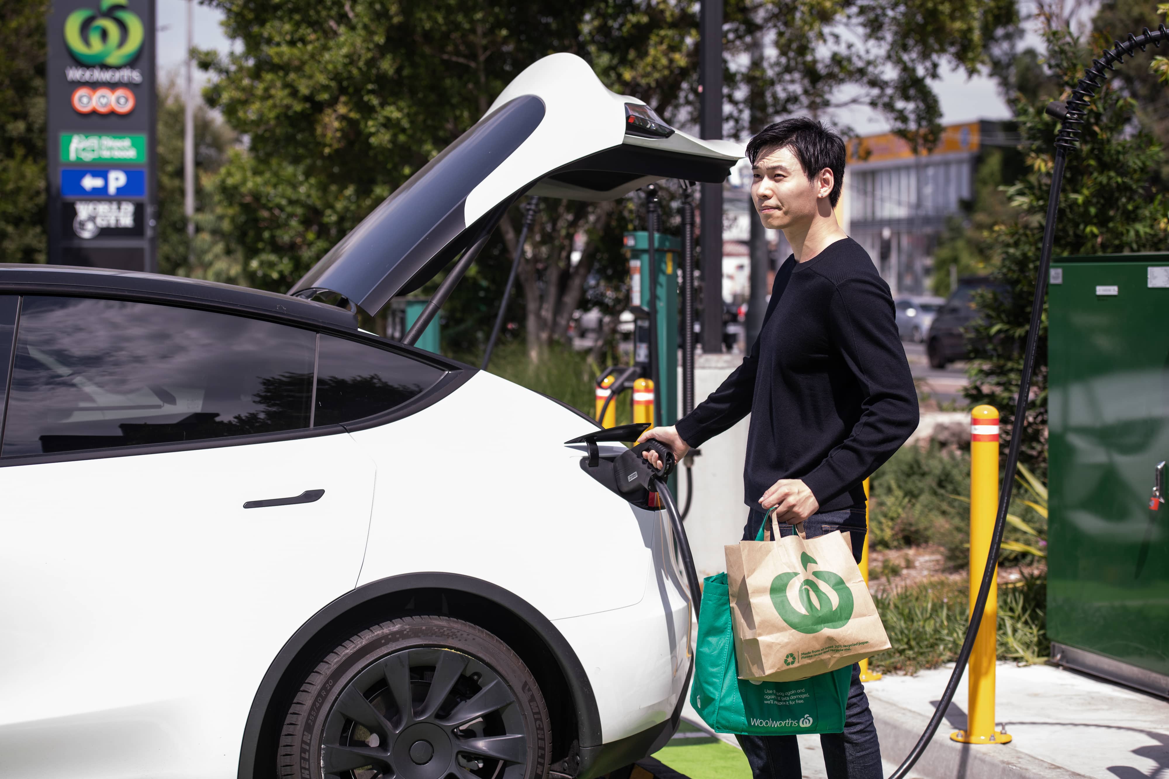 A man wearing a black sweatshirt unplugging his EV from charge after doing his groceries
