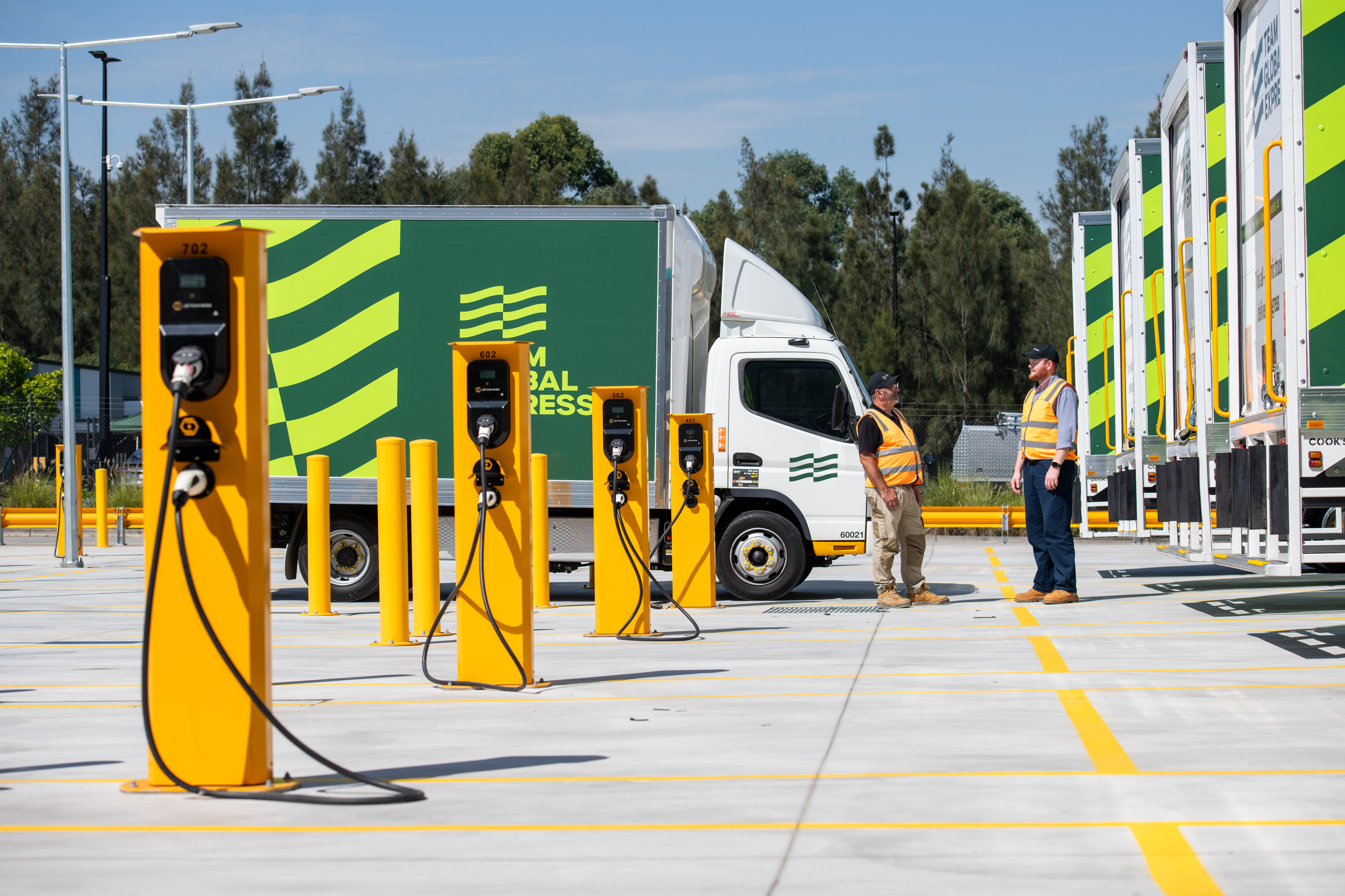 Two men stand beside a truck, engaged in charging it as part of an electric fleet incentive program.